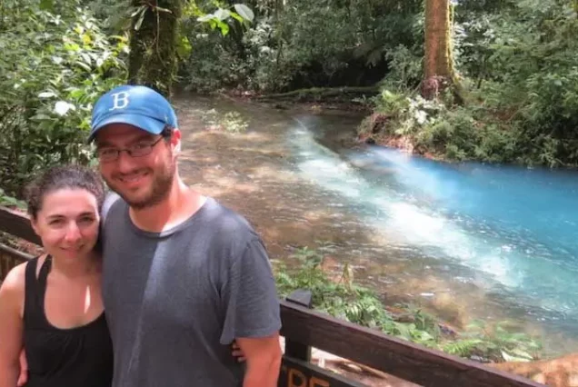 A man and woman posing in front of the stunning blue river, Rio Celeste Waterfall Hike.