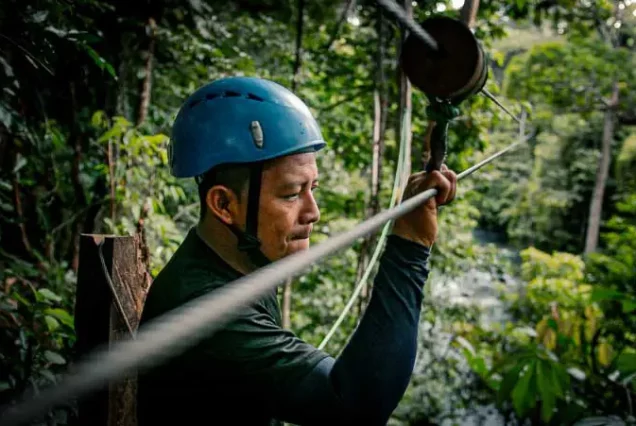 A man Rio Celeste zip-lining through the Rio Celeste jungle with a helmet on a rope.