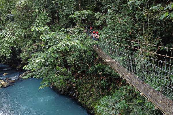 Visitors at Onca Adventure Park Costa Rica crossing a suspension bridge over a river.