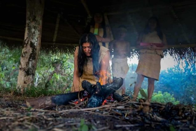 A person in Nike attire tending to a fire outdoors with three observers in the background.