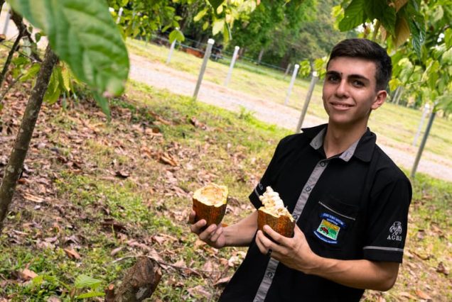 Amid the lush trees of Costa Rica, a person wearing a logo-emblazoned black shirt holds open cacao pods filled with seeds. This hands-on experience is part of the Didactic Costa Rica Farm School Tour.