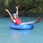 A girl on a tube on the Rio Celeste, rising her arms.