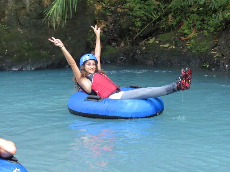 A girl on a tube on the Rio Celeste, rising her arms.