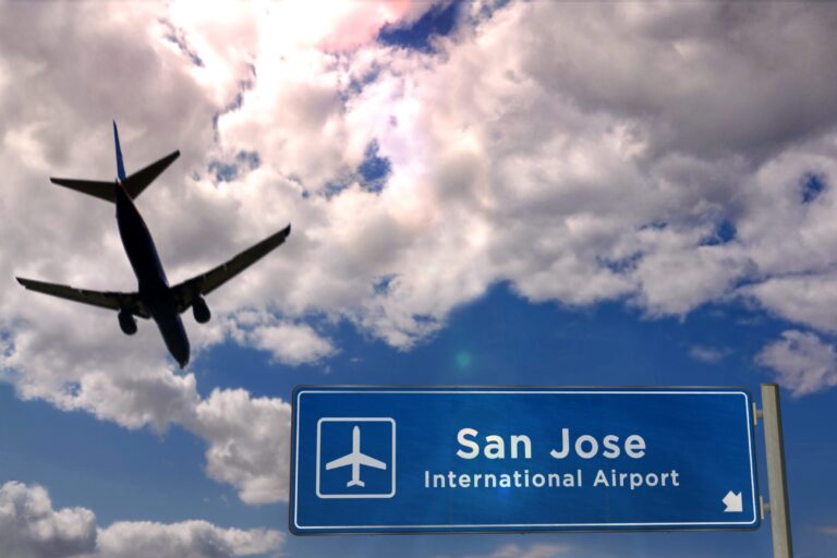 Silhouette of an airplane flying over a blue sign reading “San Jose International Airport” against a cloudy sky, evoking a sense of wanderlust where global airports connect travelers to distant lands like Costa Rica. Silhouette of an airplane flying over a blue sign reading "San Jose International Airport" against a cloudy sky, evoking a sense of wanderlust where global airports connect travelers to distant lands like Costa Rica.