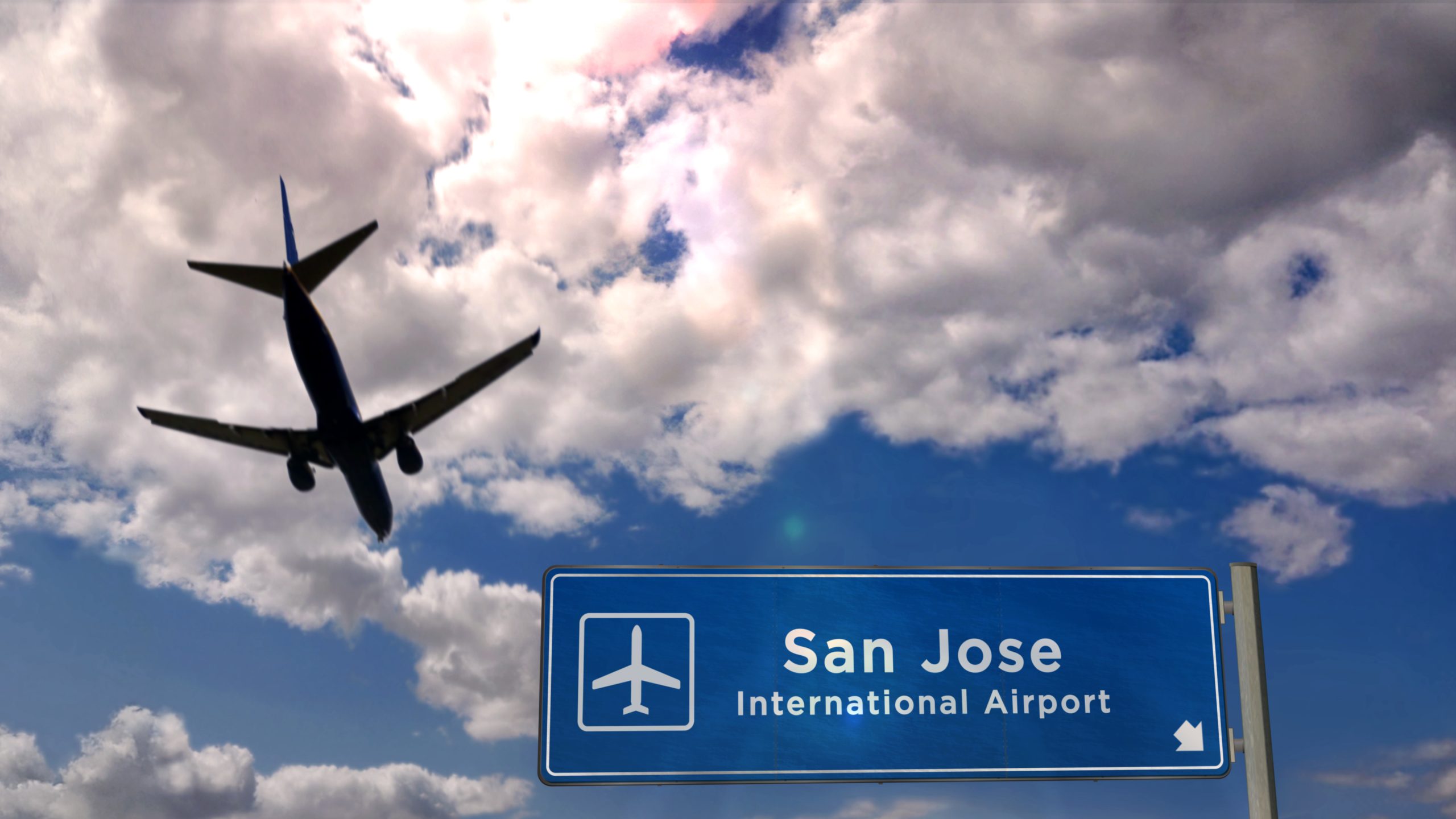 Silhouette of an airplane flying over a blue sign reading “San Jose International Airport” against a cloudy sky, evoking a sense of wanderlust where global airports connect travelers to distant lands like Costa Rica. Silhouette of an airplane flying over a blue sign reading "San Jose International Airport" against a cloudy sky, evoking a sense of wanderlust where global airports connect travelers to distant lands like Costa Rica.