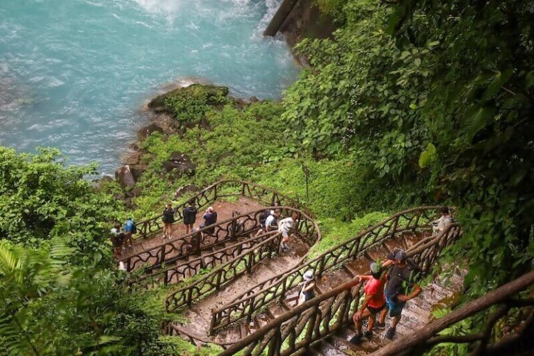 A group of people are walking up stairs to a waterfall in the Rio Celeste location. A group of people are walking up stairs to a waterfall in the Rio Celeste location.