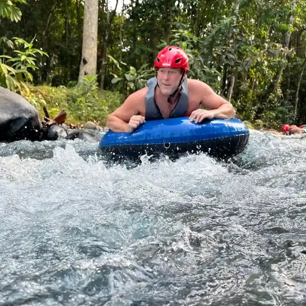 Person tubing in Rio Celeste down a rocky stream wearing a safety helmet.