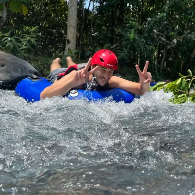Person wearing a red helmet making a peace sign while tubing in Rio Celeste.