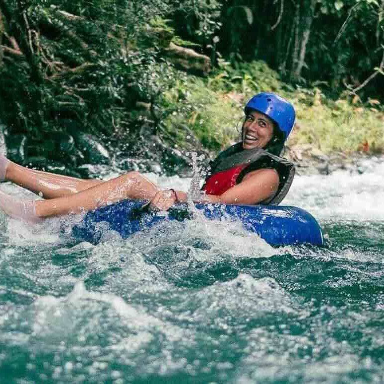 Woman in a blue helmet joyfully tubing down a fast-flowing forest river.