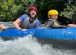 A man and a child, wearing helmets and life vests, are tubing down the mesmerizing waters of Rio Celeste, enjoying the lush greenery around them.