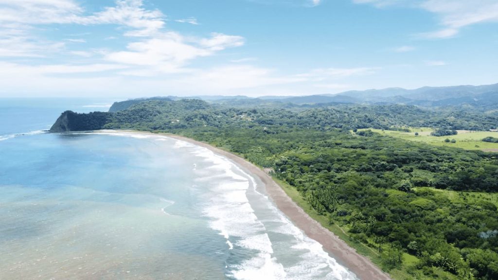 Aerial view of a coastal landscape in Costa Rica travel with pristine beaches, lush rainforests, and rolling hills under a partly cloudy sky.