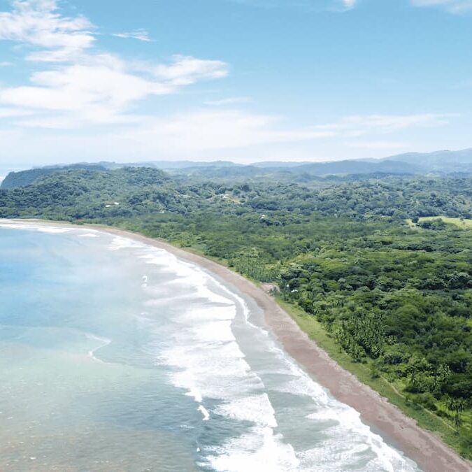 Aerial view of a coastal landscape in Costa Rica travel with pristine beaches, lush rainforests, and rolling hills under a partly cloudy sky.