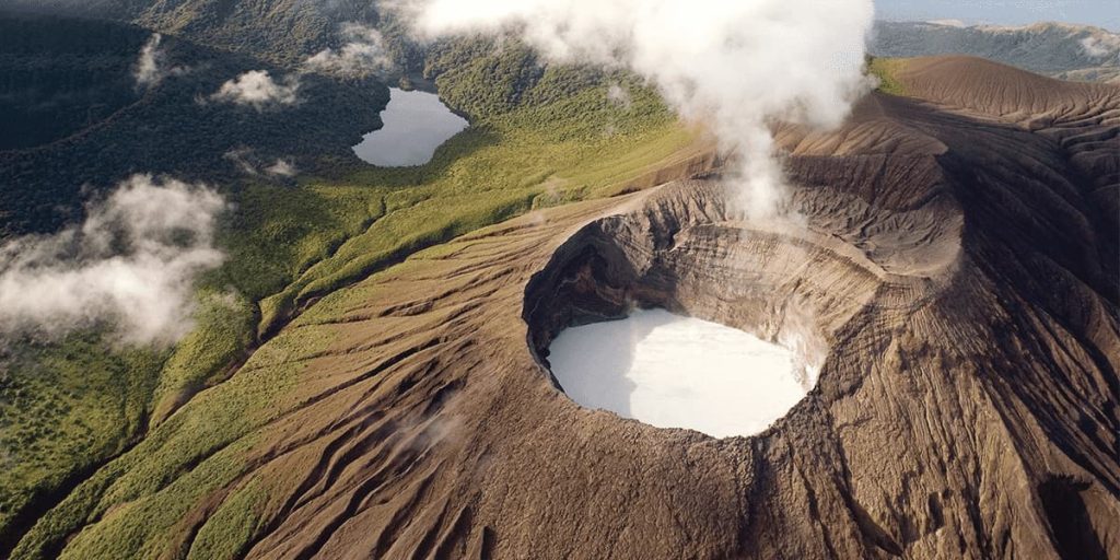 Aerial view of a volcanic crater with a white lake at its center, surrounded by lush rainforests and two smaller lakes. White clouds hover above the landscape, capturing the natural beauty typical of Costa Rica Travel.