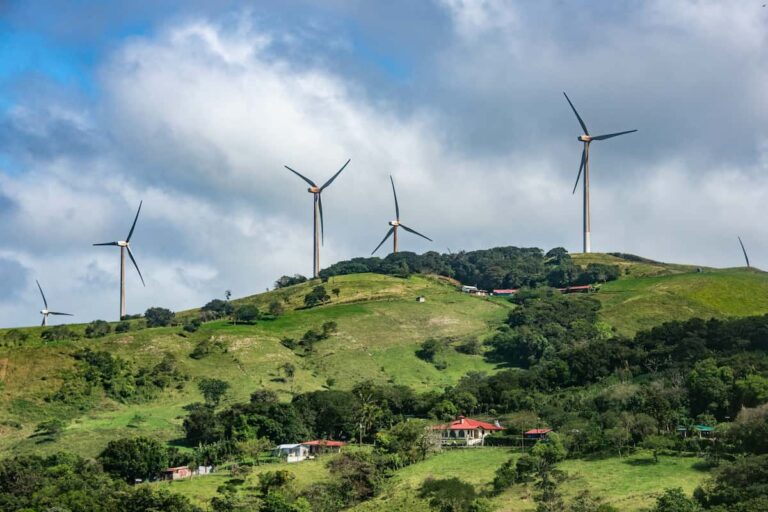 Wind turbines harness renewable energy on a lush green hillside in Costa Rica, with scattered houses and a cloudy sky as the backdrop. Wind turbines harness renewable energy on a lush green hillside in Costa Rica, with scattered houses and a cloudy sky as the backdrop.