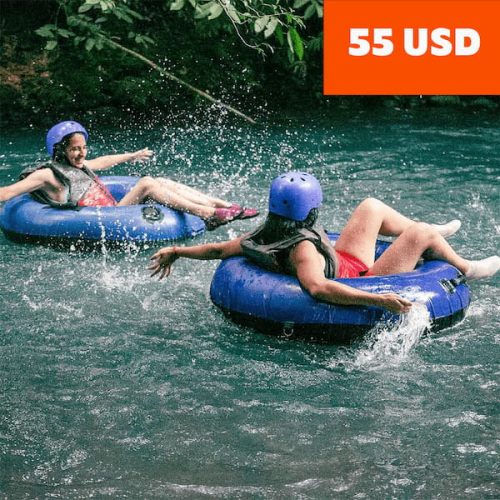 Two people wearing helmets float on blue tubes in a river, with splashes of water dancing around them. Nearby, the allure of Rio Celeste hiking beckons adventurers. A price tag in the corner reads "55 USD. Two people wearing helmets float on blue tubes in a river, with splashes of water dancing around them. Nearby, the allure of Rio Celeste hiking beckons adventurers. A price tag in the corner reads "55 USD.