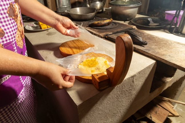 In a rustic kitchen setting reminiscent of an Adventure Park in Costa Rica, a person skillfully presses tortillas with a wooden press, each one akin to embarking on a culinary challenge course.
