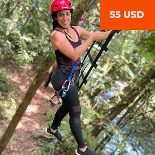 A woman wearing a red helmet and climbing harness steps onto a rope bridge in a forest, with a price tag of 55 USD in the corner. A woman wearing a red helmet and climbing harness steps onto a rope bridge in a forest, with a price tag of 55 USD in the corner.
